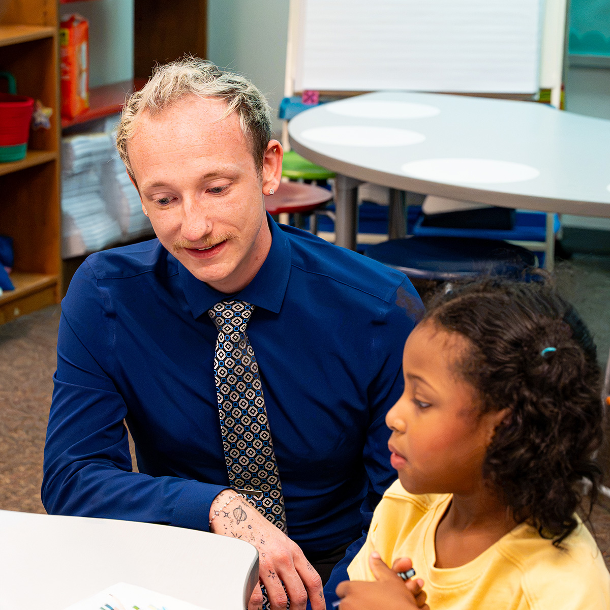 Teacher Alex Reid working with a student in a classroom.
